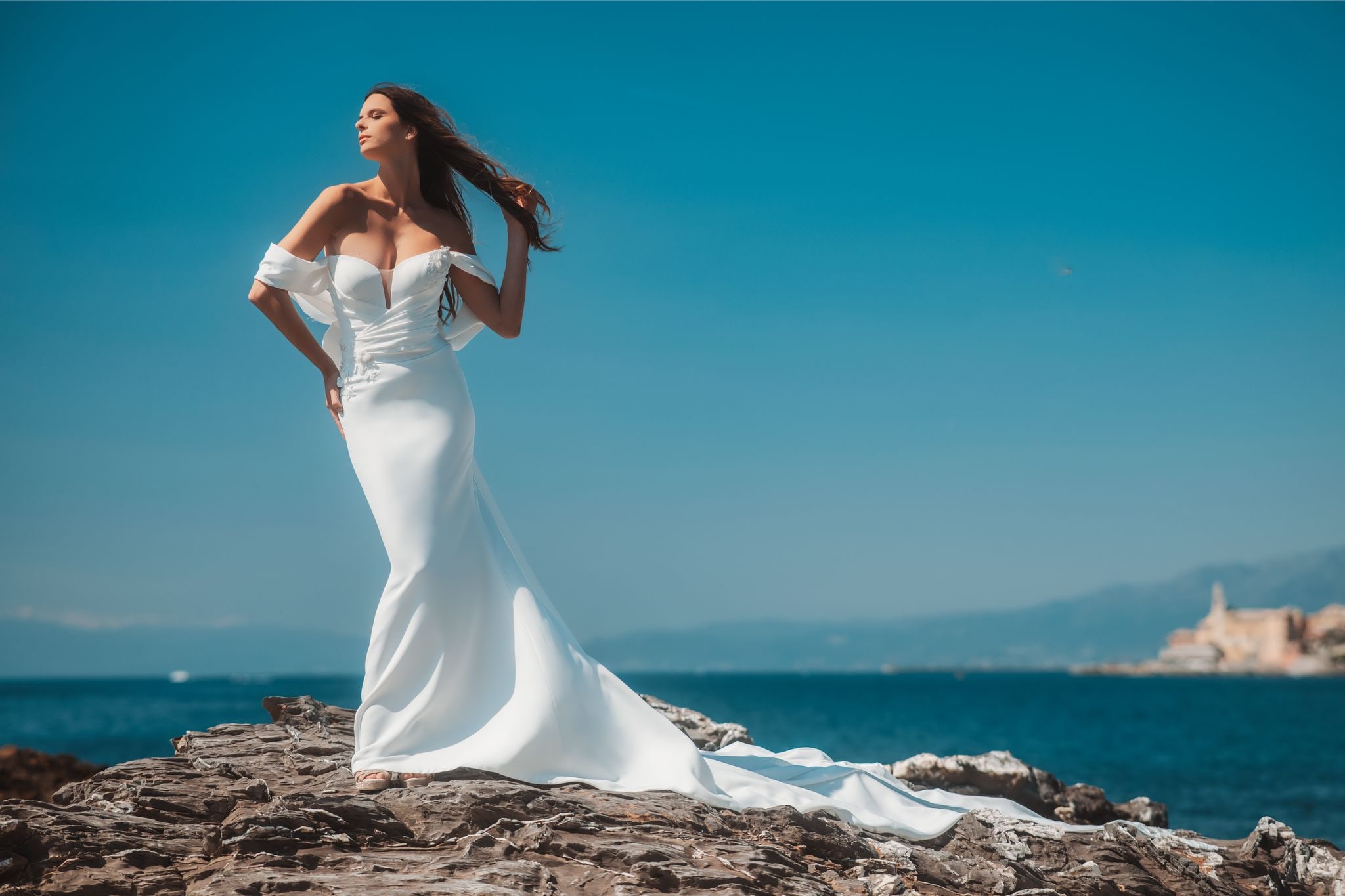 Sposa in abito bianco su scogliera davanti al mare.